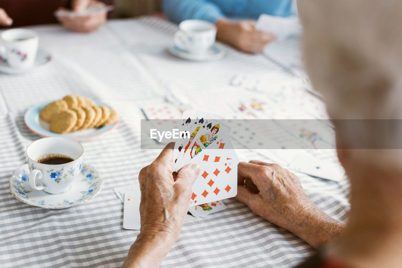 Cropped image of senior woman playing cards with family at table