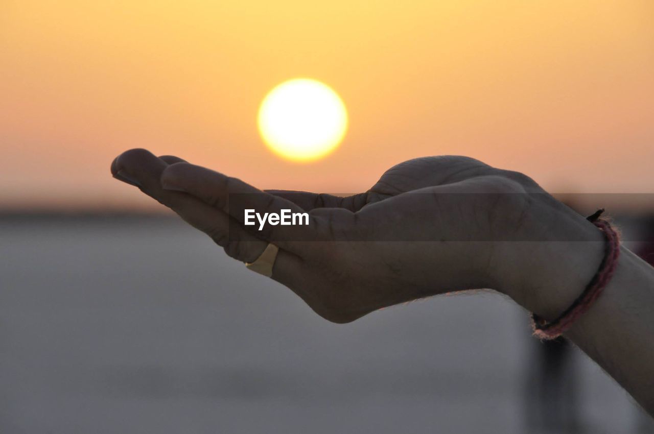 Close-up of hand against sun during sunset