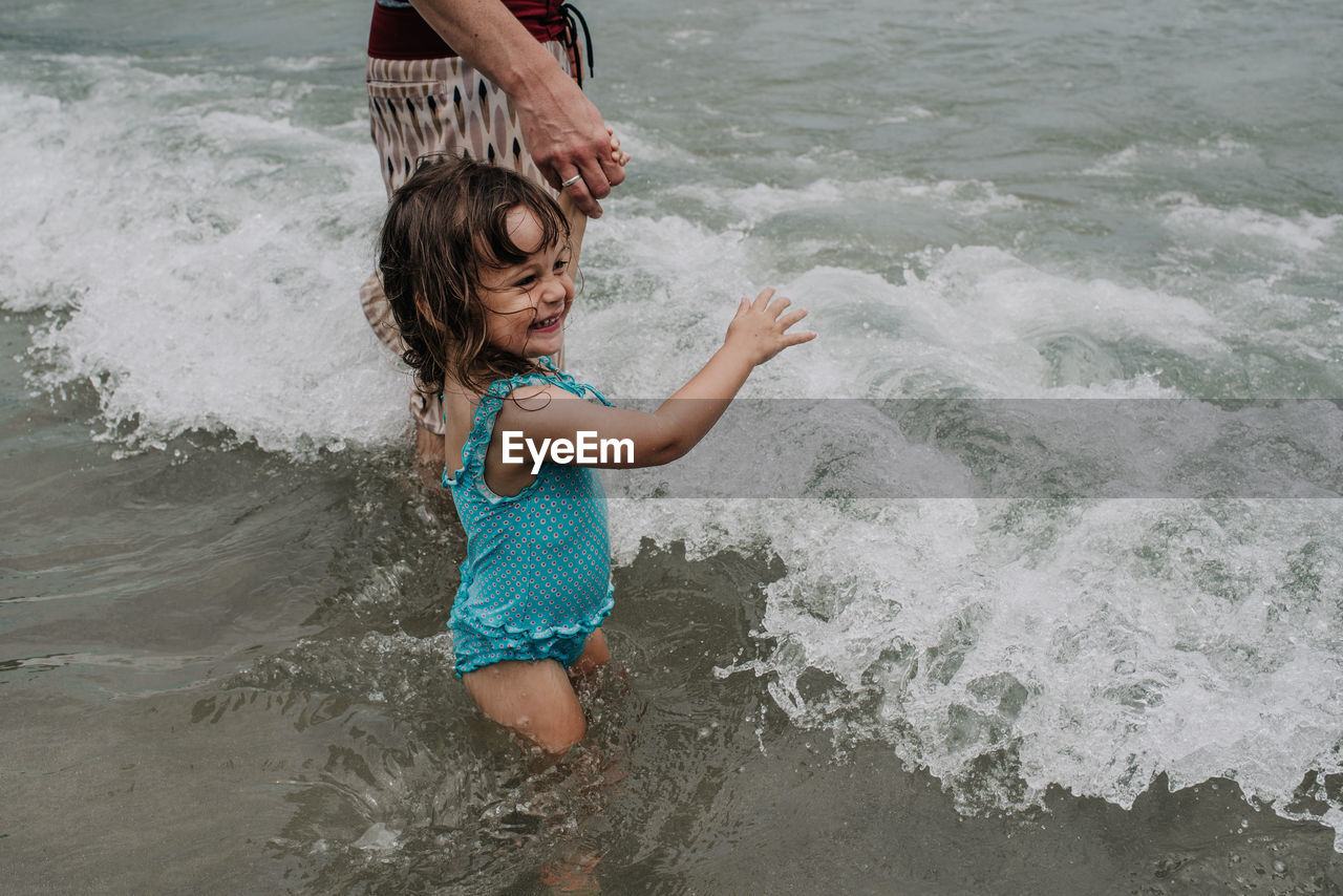 Cheerful daughter holding mother hand while playing in sea