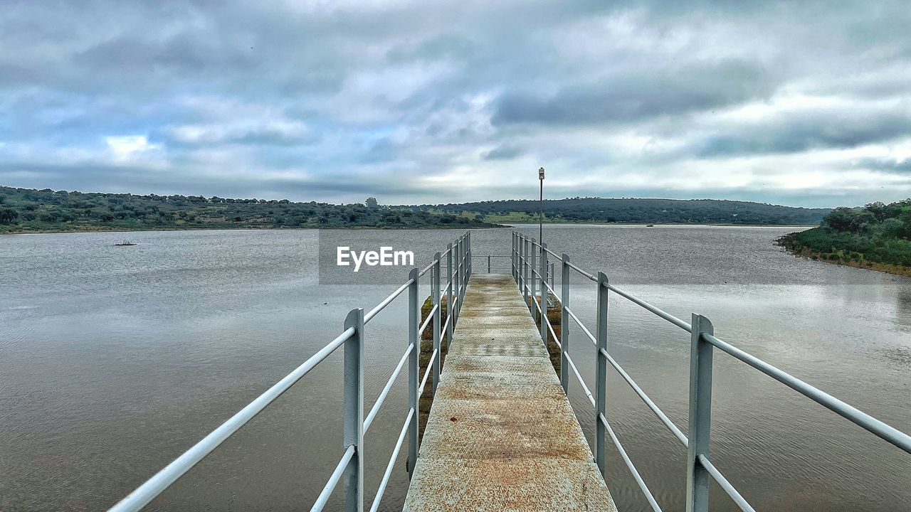 water, cloud, sky, the way forward, nature, environment, sea, architecture, scenics - nature, land, beauty in nature, landscape, railing, transportation, bridge, tranquility, no people, diminishing perspective, beach, built structure, travel, shore, outdoors, tranquil scene, travel destinations, reservoir, day, vanishing point, coast, footpath, tourism, non-urban scene, overcast, pier, waterway, walkway, dramatic sky, cloudscape, horizon, footbridge, holiday, road, trip