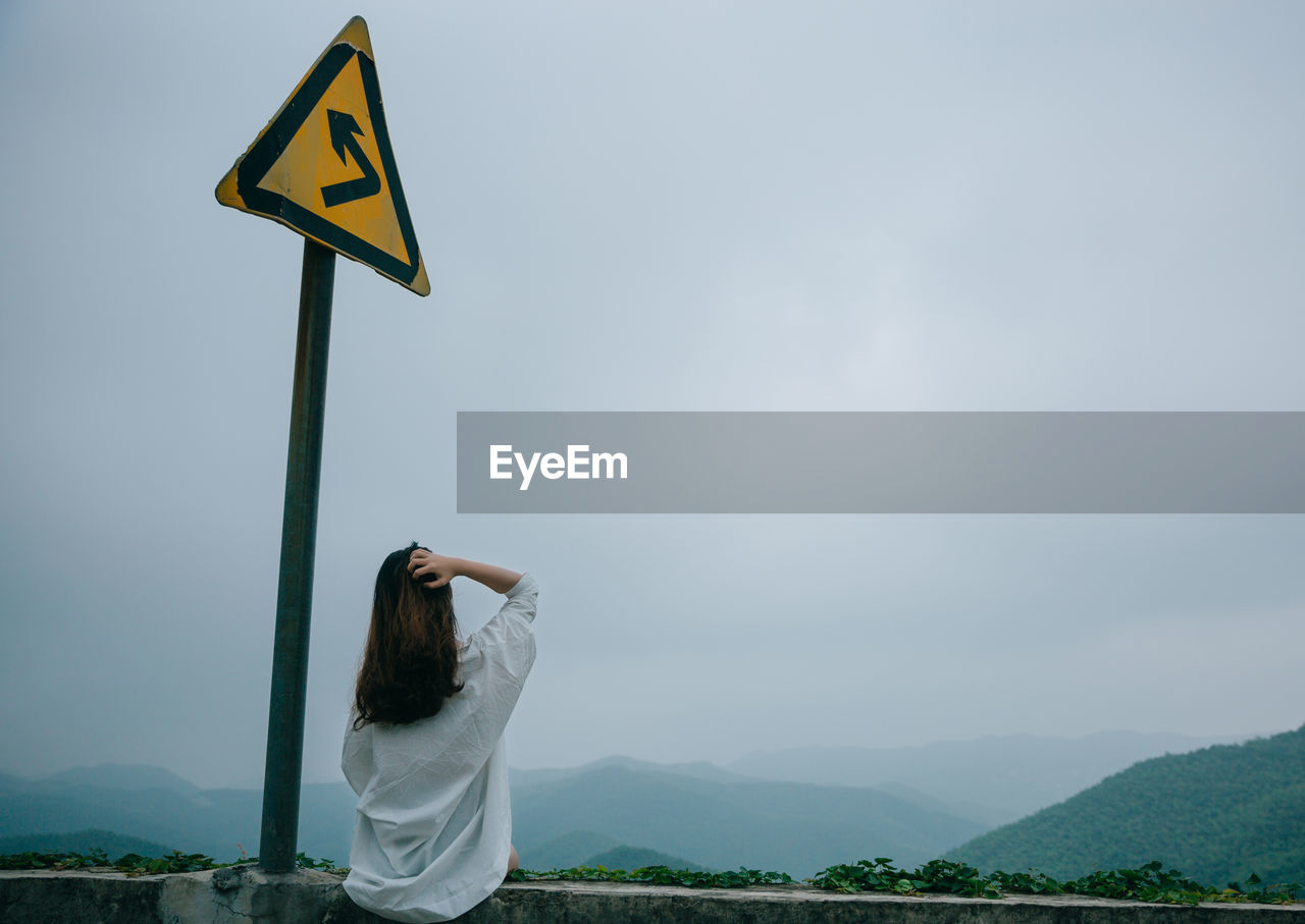 Rear view of woman standing by information sign against sky