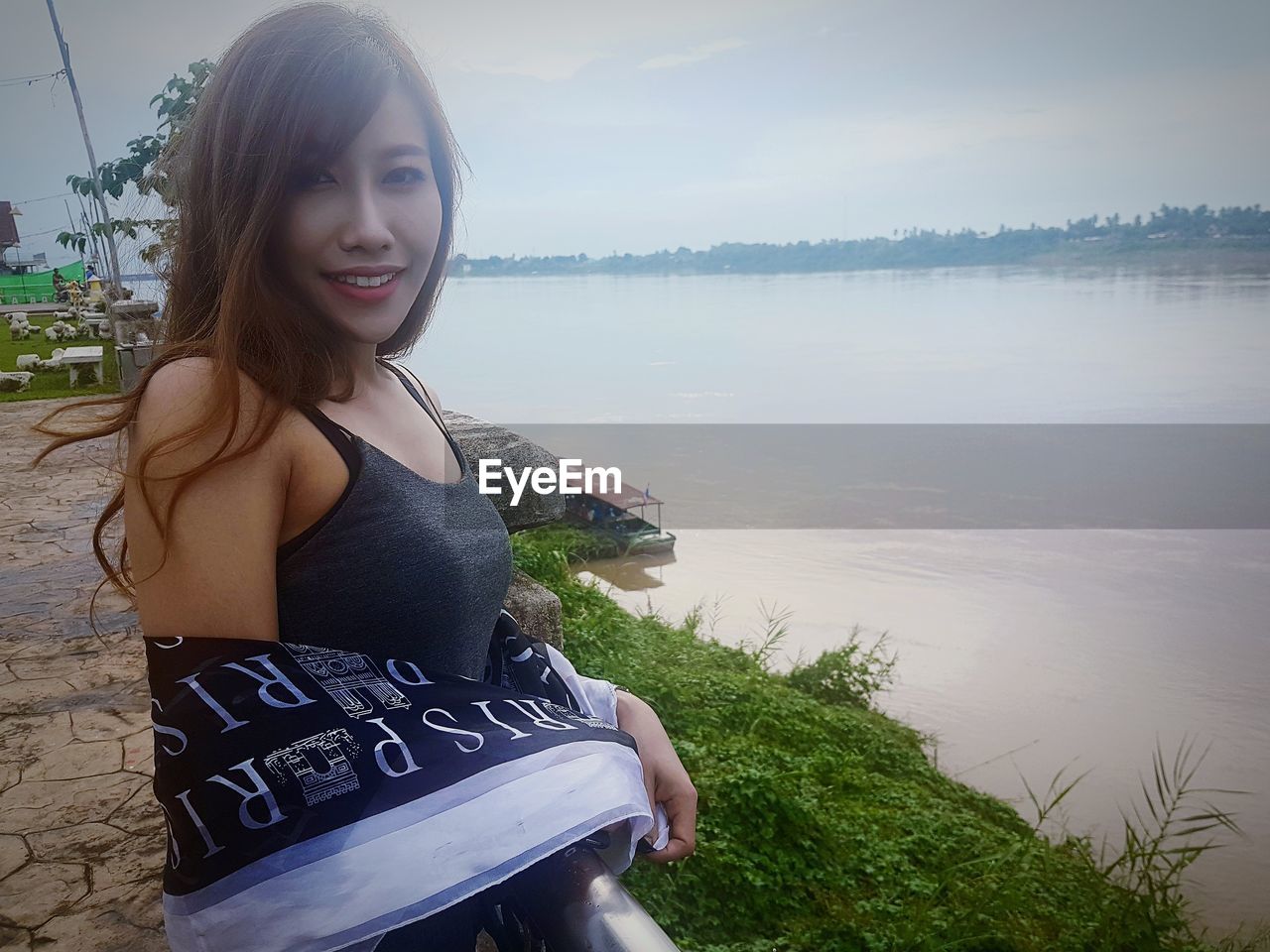 Portrait of smiling woman standing on lakeshore against sky