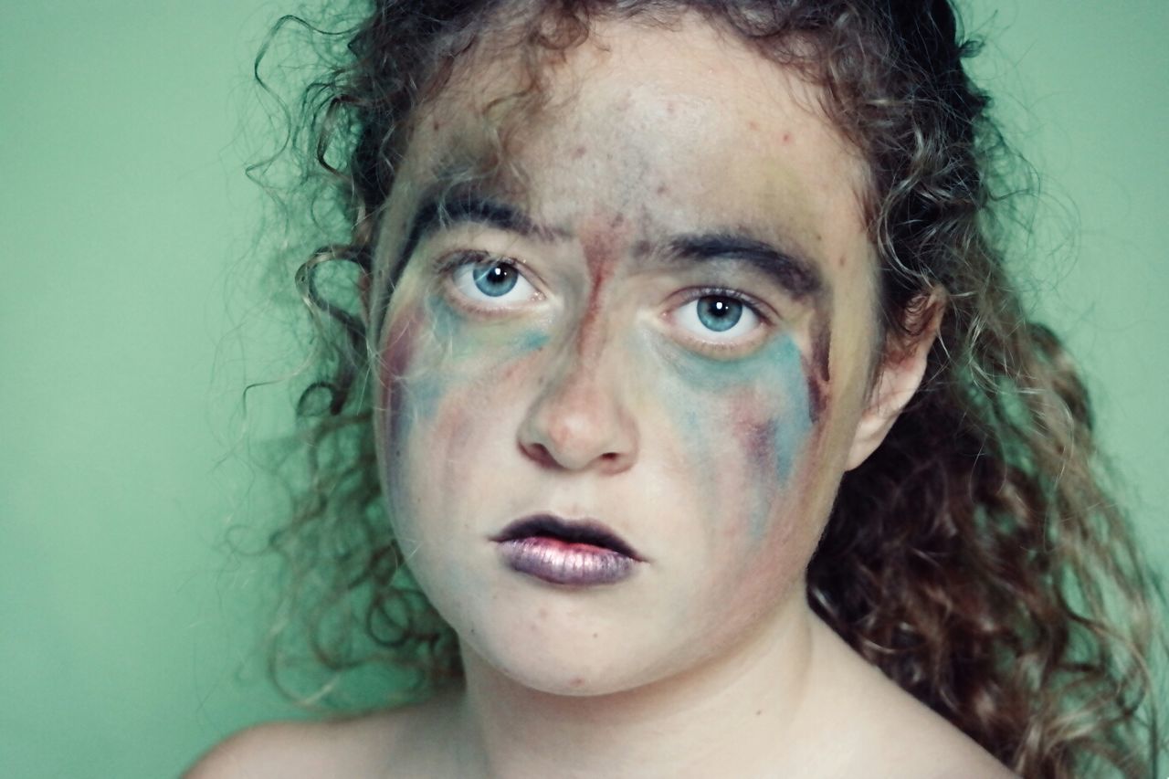 Portrait of young woman with messy make-up on her face against green background