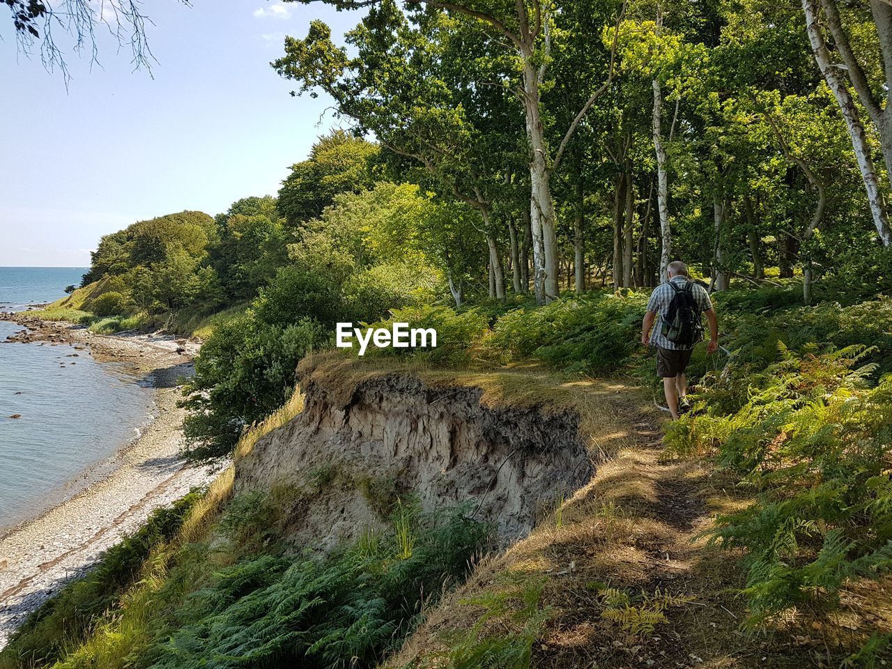 REAR VIEW OF MAN WALKING BY WATER