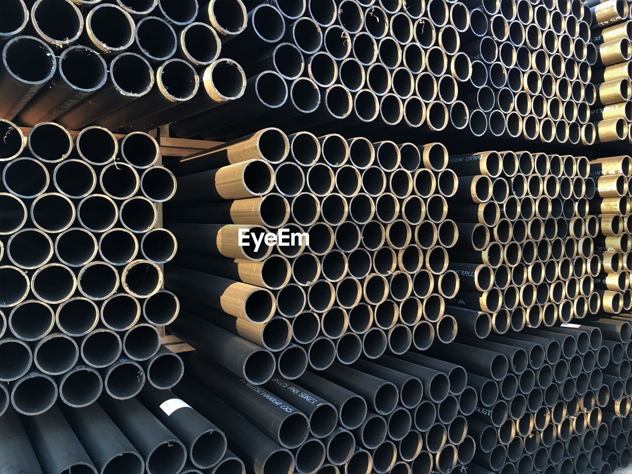 Full frame shot of stacked pipes at factory during sunset