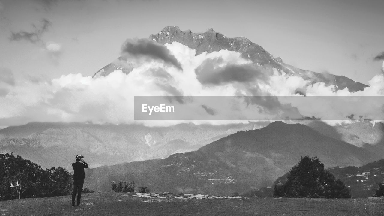 Rear view of man standing on mountain against sky