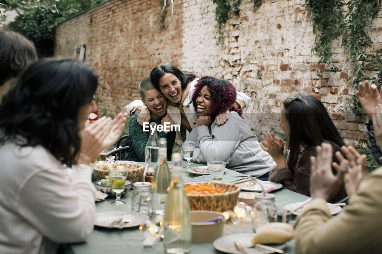 Multiracial female friends laughing together during dinner party in back yard