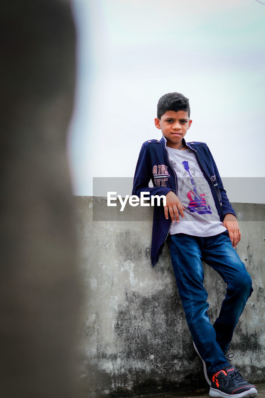 Portrait of young boy standing against wall
