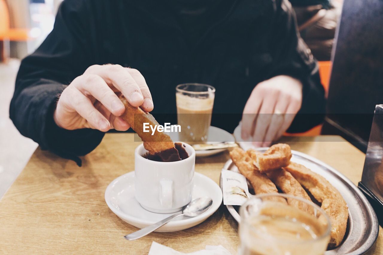 Close-up of man eating and dipping churros in chocolate in a cafeteria 