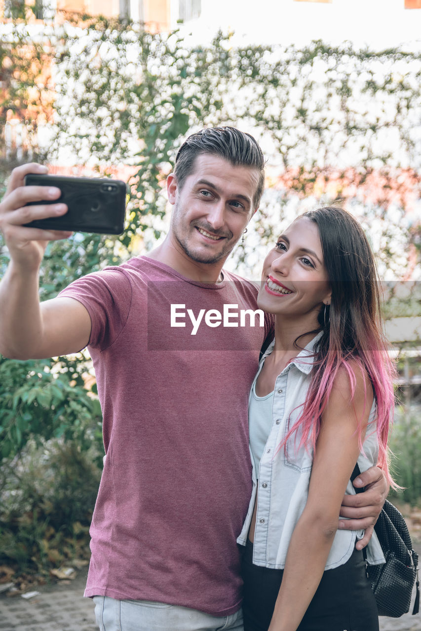 A portrait of brunette young couple smiling and taking selfie photo while walking outdoors