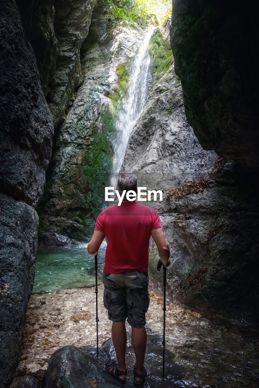 A hiker in the gorge surrounded by rocks in front of the waterfall.