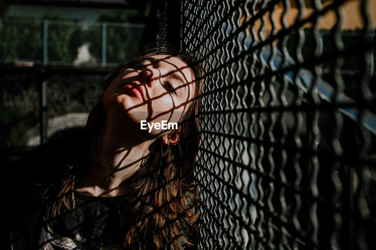 fence, one person, black, chainlink fence, darkness, long hair, young adult, hairstyle, women, portrait, adult, light, headshot, sadness, leisure activity, lifestyles, fashion, wire mesh, outdoors, wire, spring, chain-link fencing, mesh, nature, looking, wire fencing, emotion, focus on foreground, metal, depression - sadness, casual clothing, person, architecture, loneliness, day, security