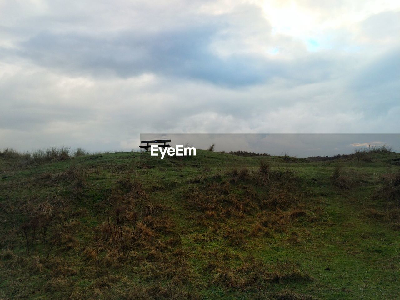 Low angle view of empty bench on grassy field against cloudy sky