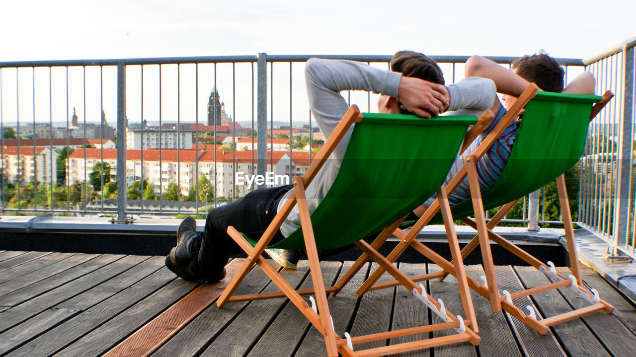 Rear view of friends relaxing on deck chair at porch