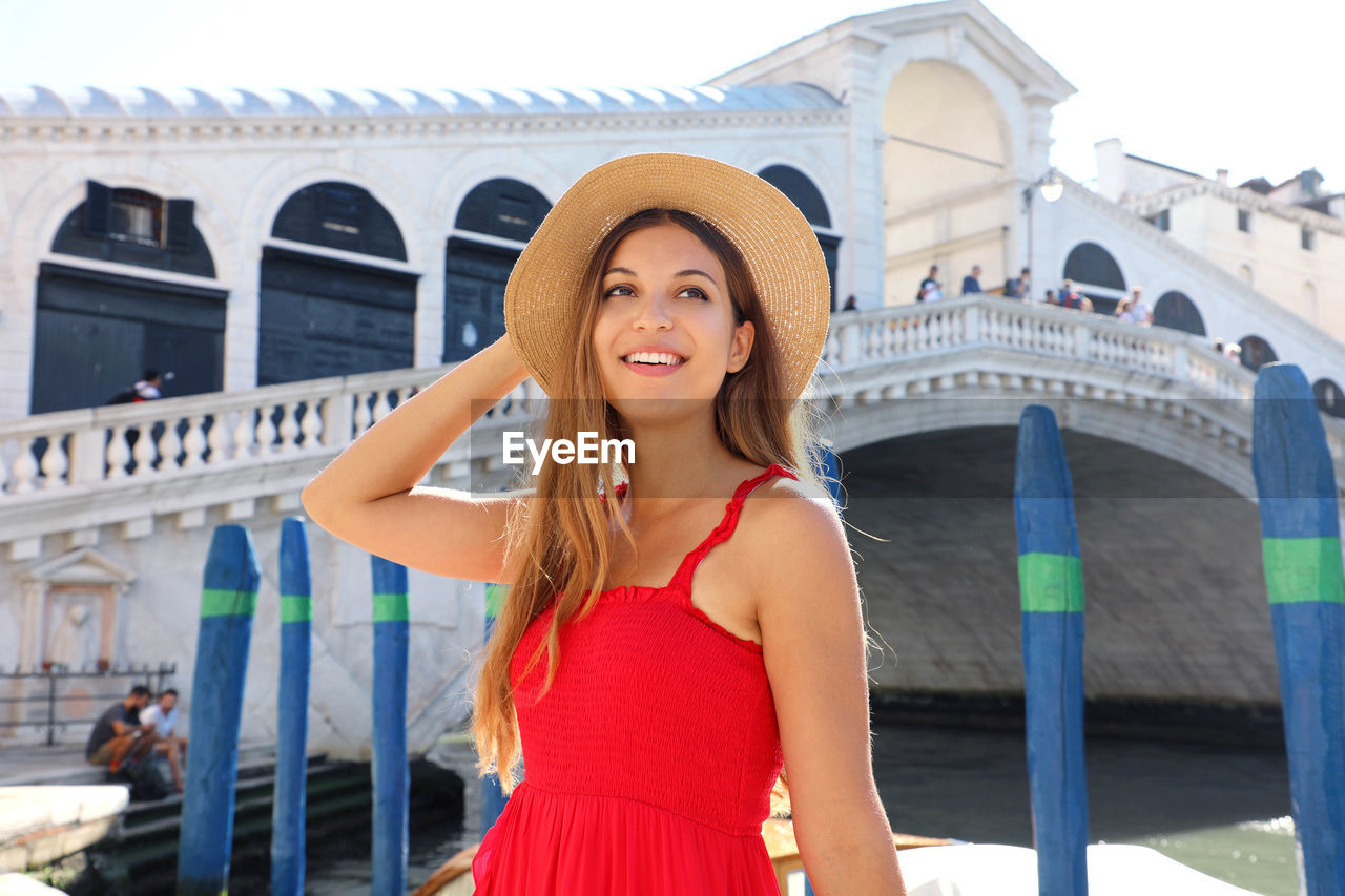 PORTRAIT OF HAPPY WOMAN STANDING AGAINST BUILDING