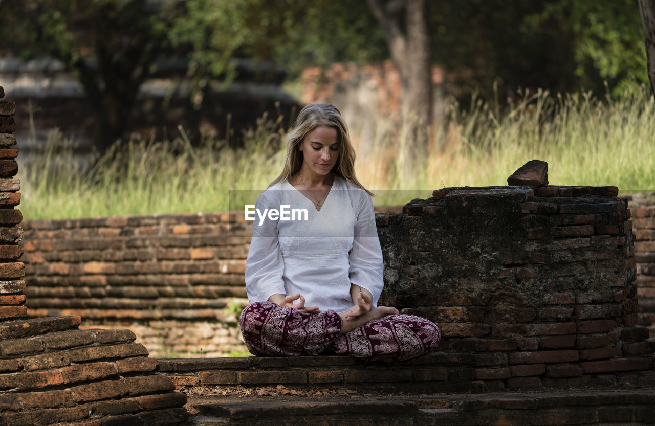 Woman mediating while sitting on brick wall