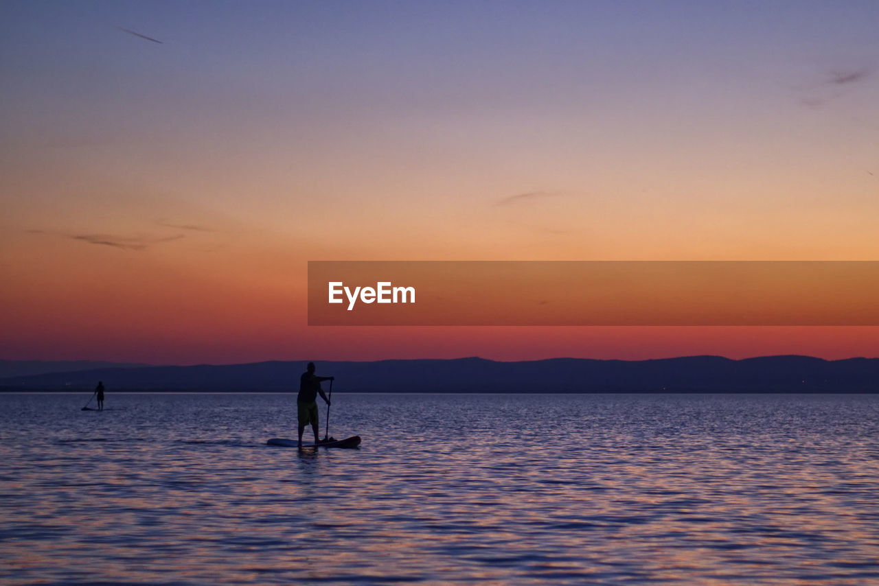 SILHOUETTE MAN ON SEA AGAINST SKY DURING SUNSET