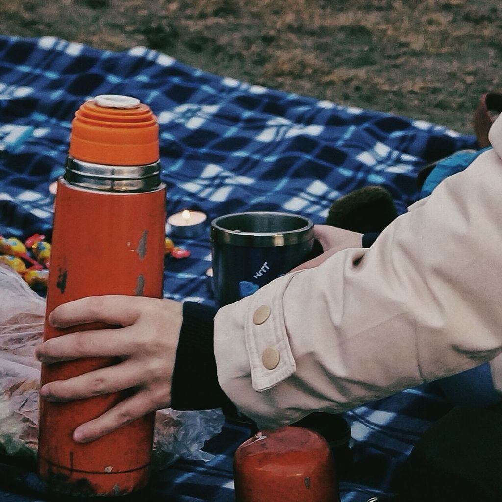 Cropped image of hand holding insulated drink container at picnic