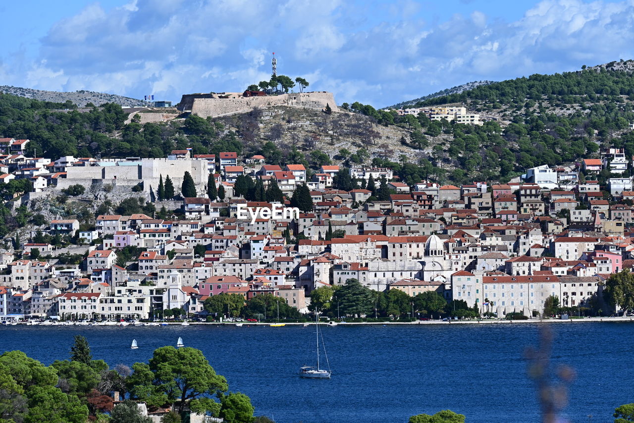 architecture, building exterior, water, town, built structure, building, city, sea, residential district, nature, sky, house, travel destinations, cityscape, land, coast, vacation, travel, mountain, nautical vessel, beach, community, aerial photography, tourism, tree, harbor, crowd, high angle view, crowded, day, plant, transportation, outdoors, coastline, cloud, landscape, village, mode of transportation, environment, blue, ship, roof, scenics - nature, townscape, the past, trip, history