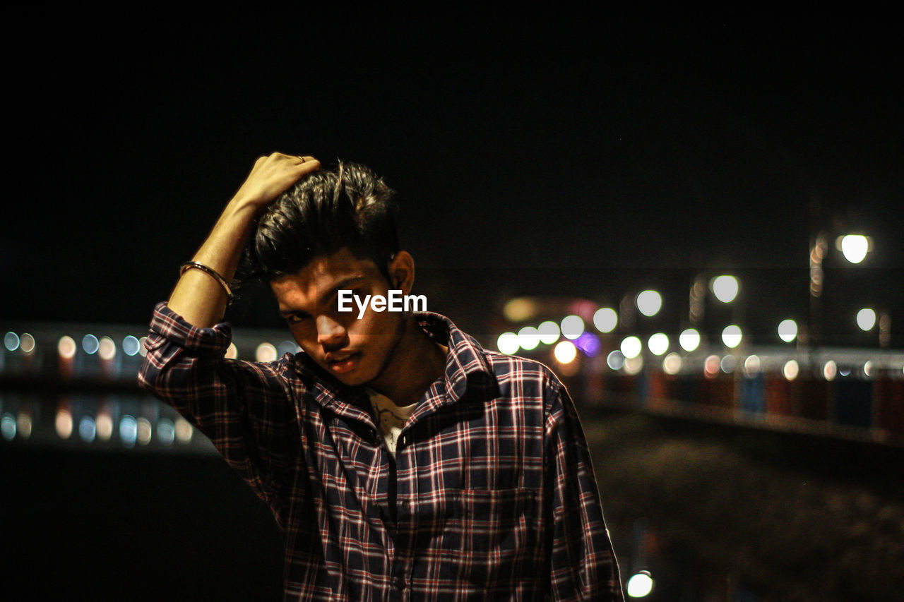 PORTRAIT OF YOUNG MAN LOOKING AT ILLUMINATED CITY