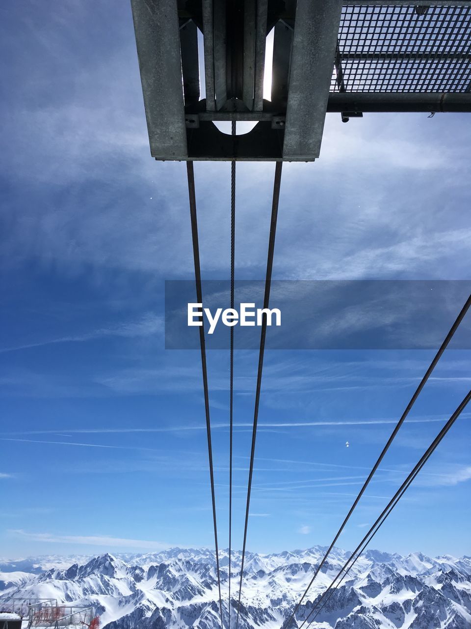 Low angle view of cables towards snowcapped mountains against sky