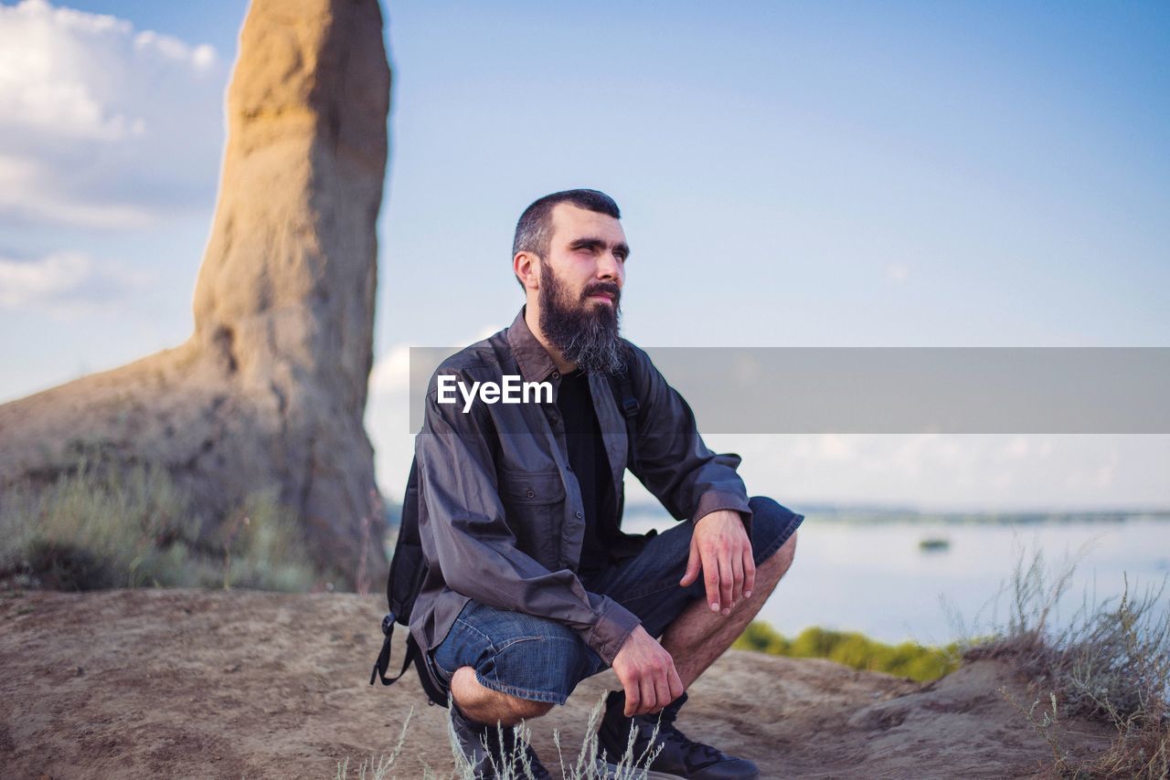 Portrait of a man in sneakers and shorts against a background of blue clear sky and mountains