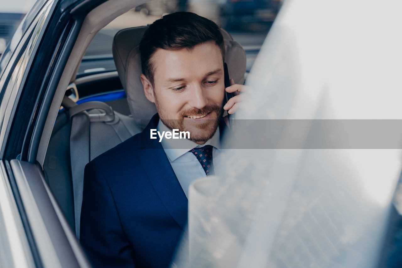 Close-up of smiling businessman talking on phone sitting at car