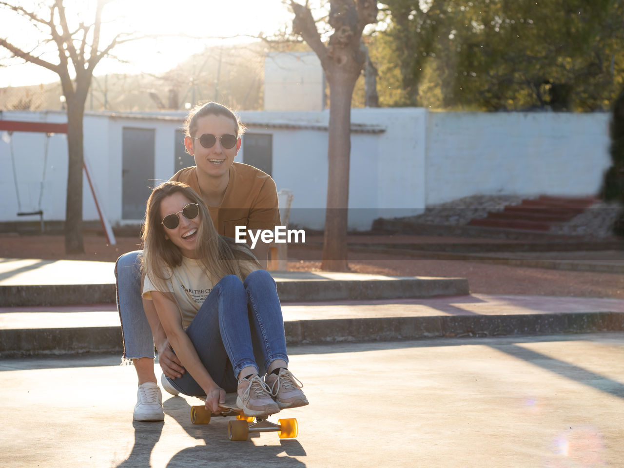 Summer love between a couple of teenagers having a good time on a skate board in the city park