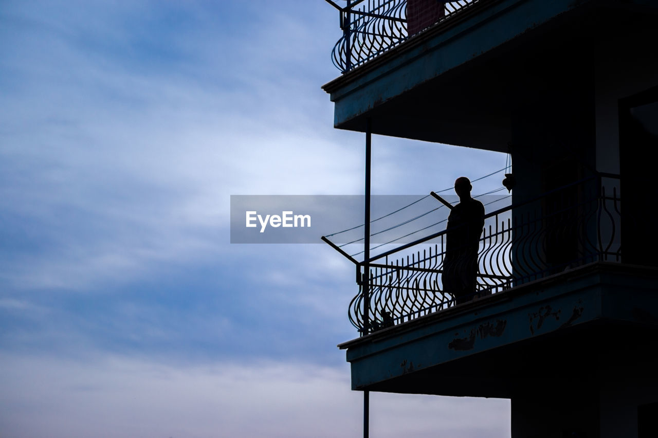 Low angle view of silhouette man standing on balcony against sky at dusk