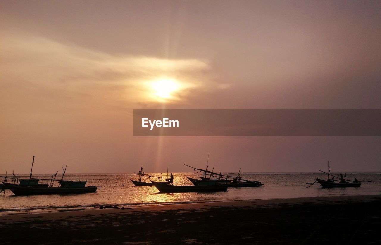 Silhouette boats moored in sea against sky during sunset