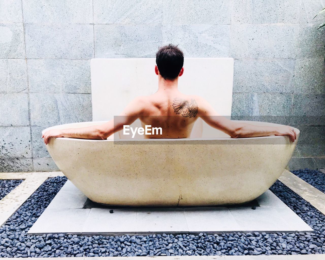 Rear view of shirtless man sitting in bathtub