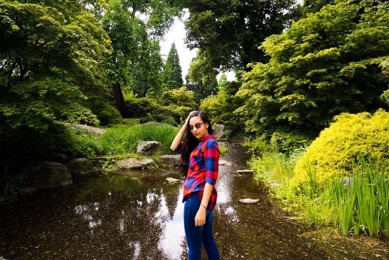 Young woman standing against stream amidst trees at park