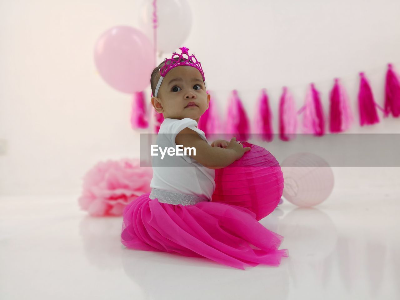 Cute baby girl in dress with decoration siting on white background