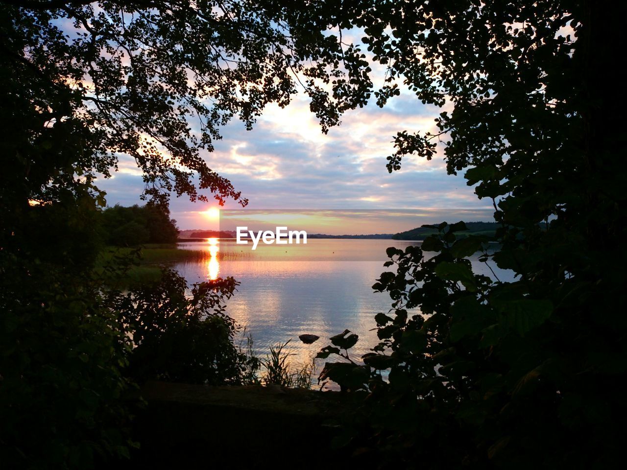 Scenic view of lake against cloudy sky at sunset
