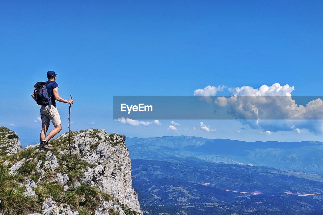 Backpacker looking at view while standing on cliff against sky during sunny day