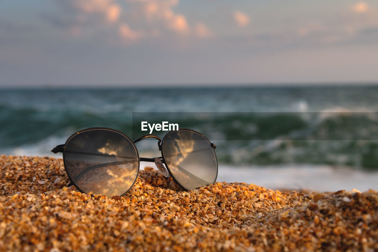 On the beach, sunglasses lie on the sand in the background a wave rolls from the sea. close-up of
