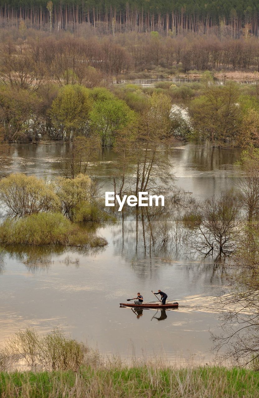 Spring scene with river in high water, trees standing in the water, people kayaking in the distance.