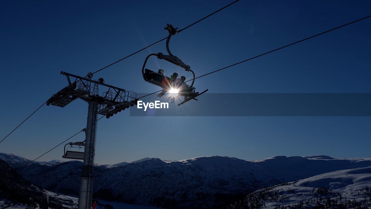 Low angle view of ski lifts over mountains against clear blue sky