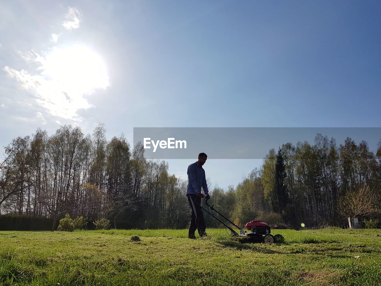 Man cleaning field with lawn mower against sky