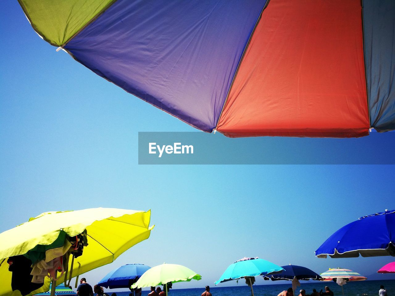 Colorful parasols and people at beach against clear blue sky