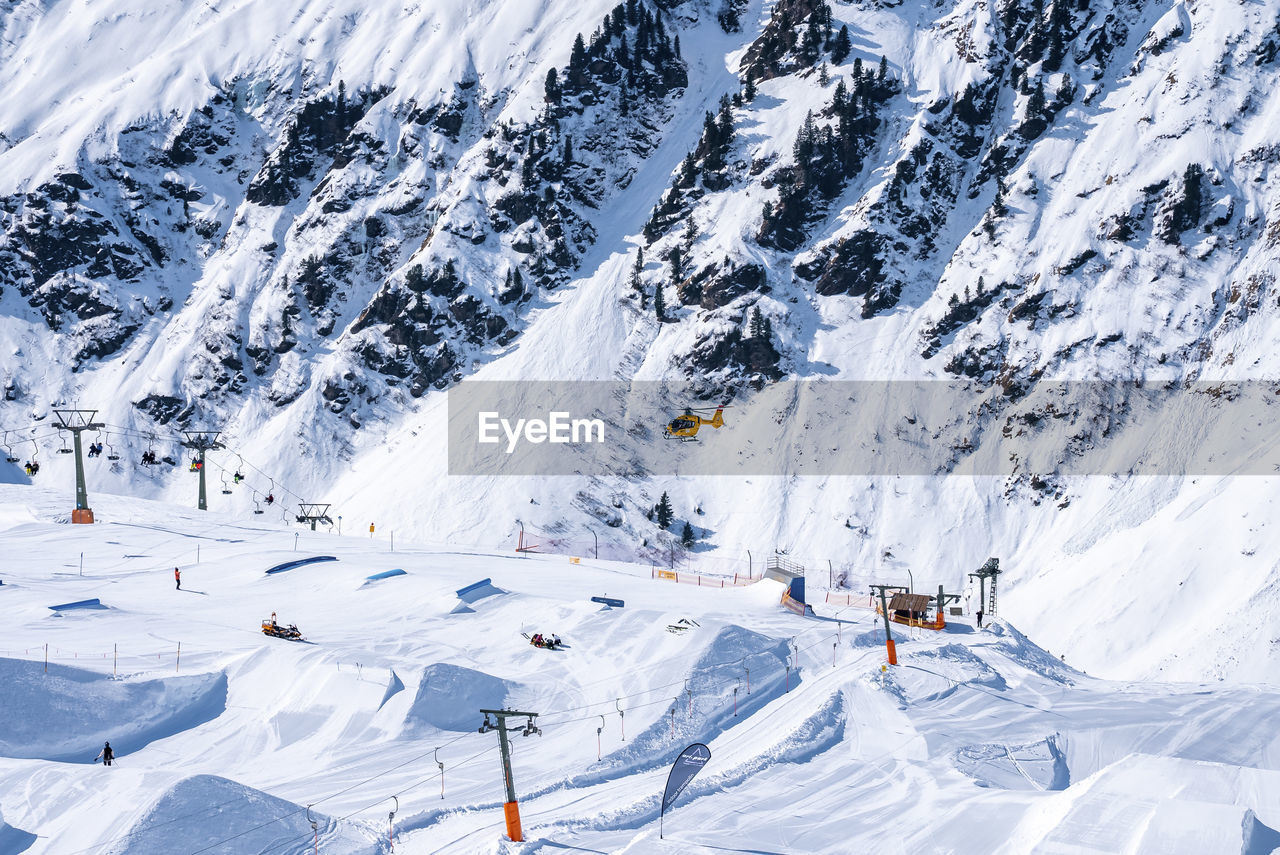 Rescue helicopter flying over skilift and drag lift on snow covered mountains