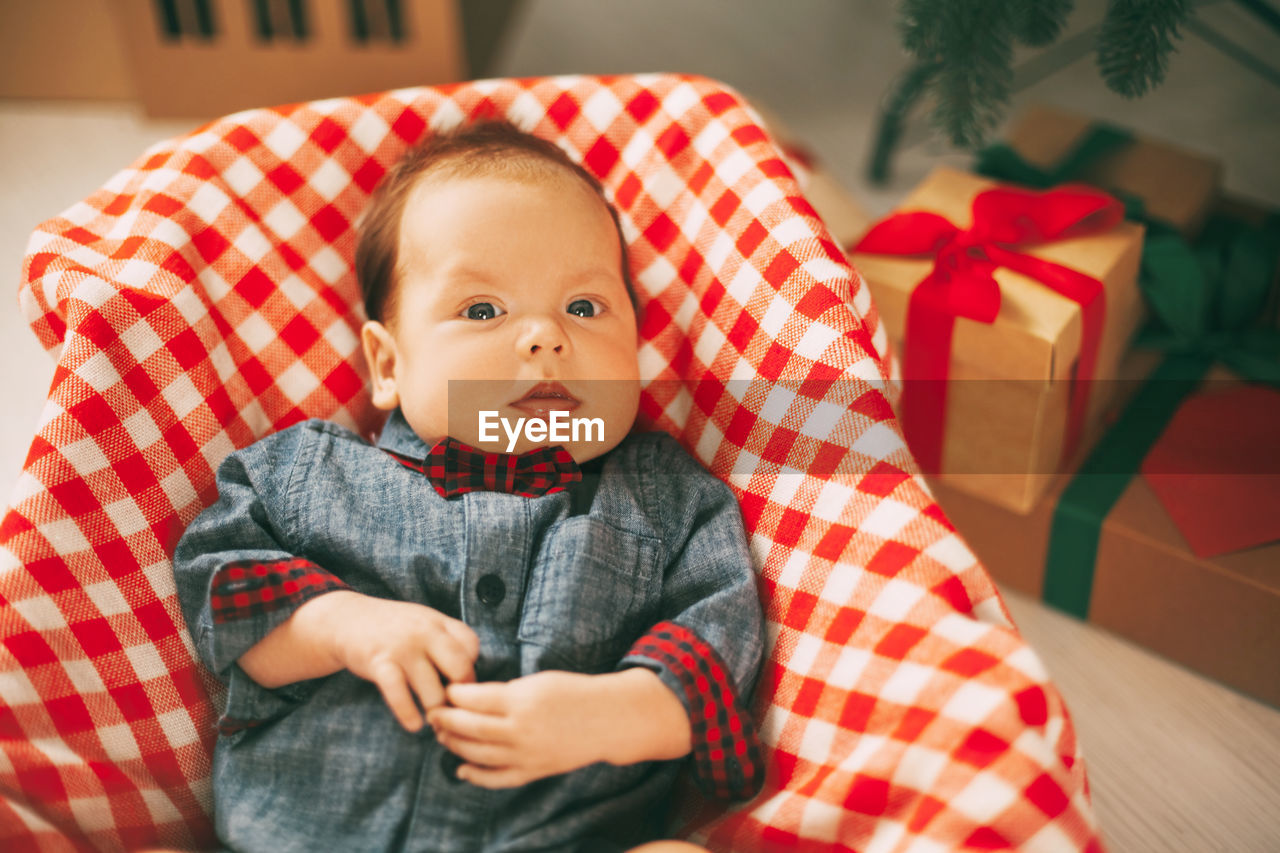 A small child is lying on a bright plaid blanket next to a christmas tree. 