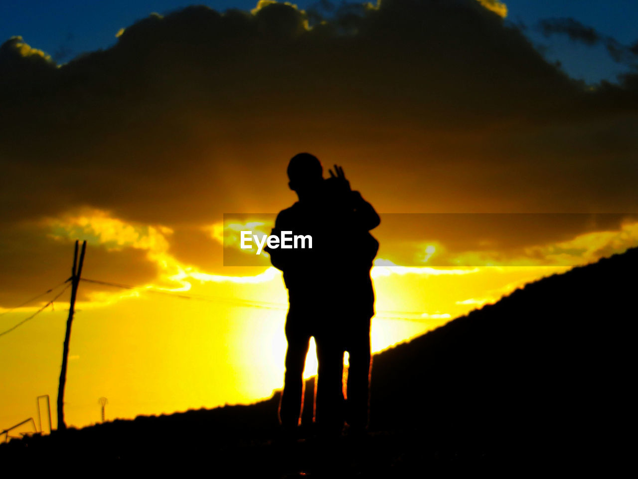 SILHOUETTE MAN PHOTOGRAPHING AGAINST ORANGE SUNSET SKY