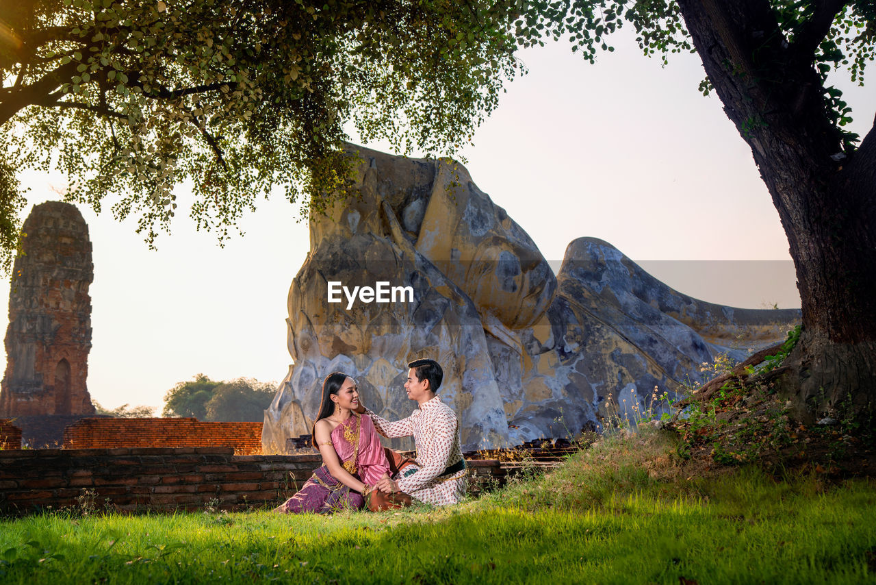 Couple sitting in park against sky