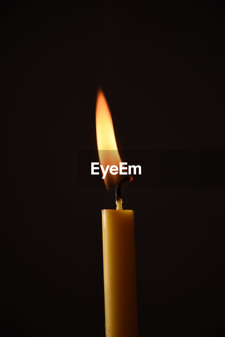CLOSE-UP OF BURNING CANDLE IN DARKROOM