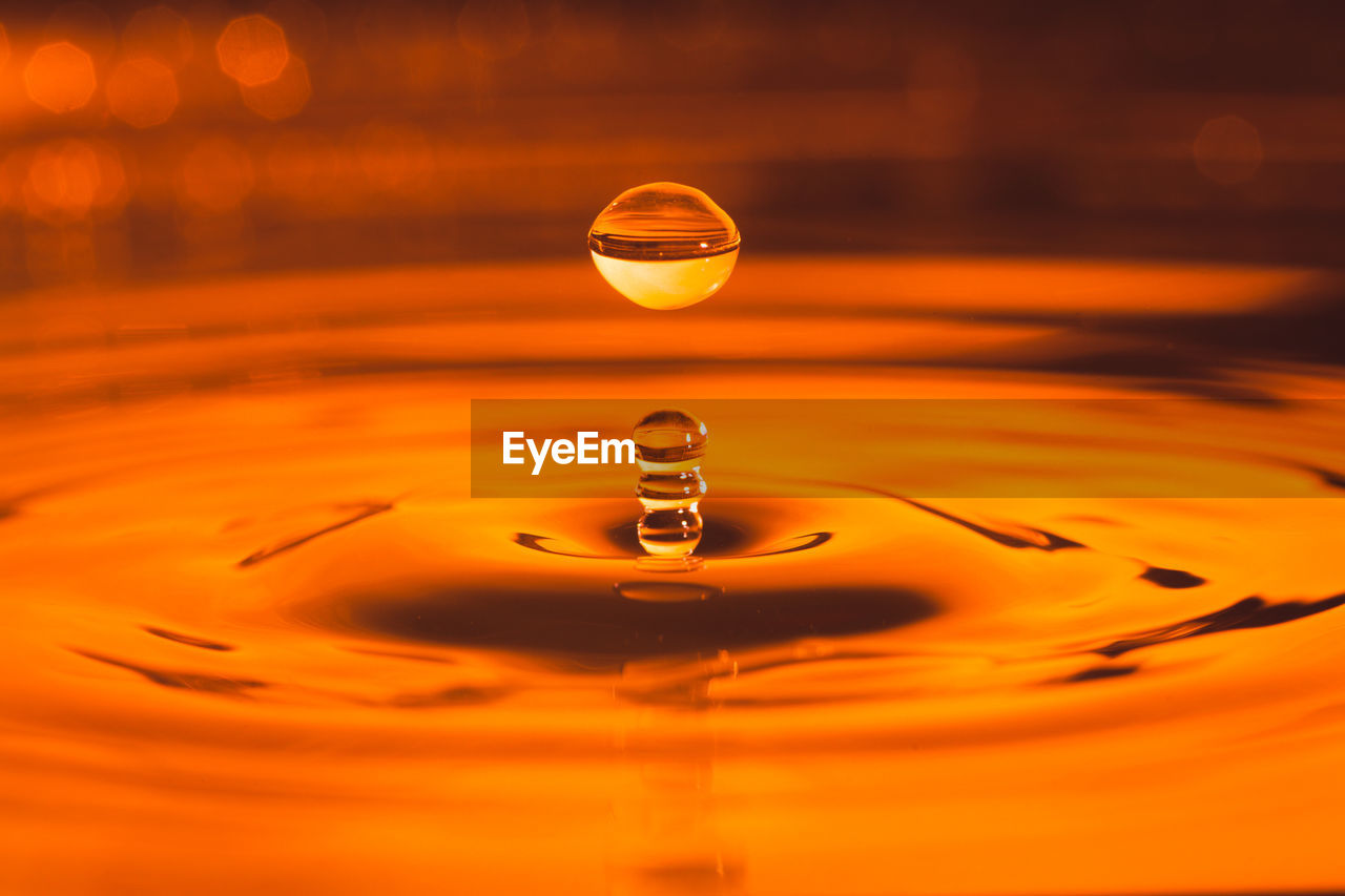 CLOSE-UP OF DROP ON RIPPLED WATER AGAINST BLURRED BACKGROUND