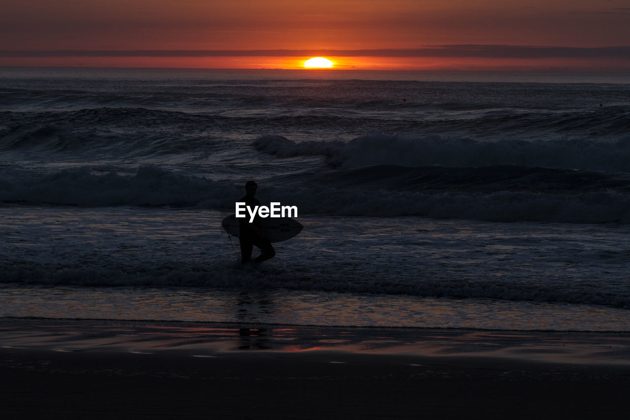 Silhouette man surfing on beach against sky during sunset