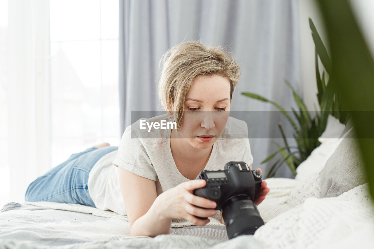 Young woman using digital camera while lying on bed at home