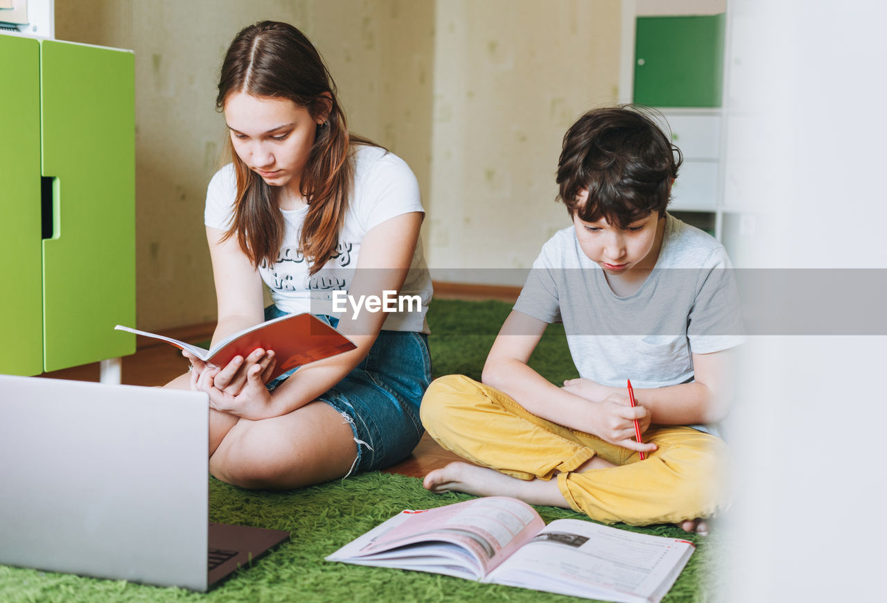 Siblings brother sister teenager and tween boy  writing in pupil book with opened laptop 