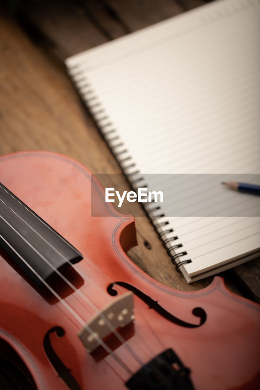 High angle view of violin by spiral notebook and pencil on table